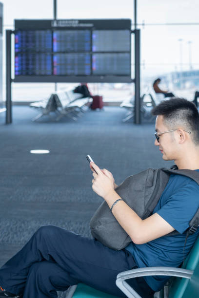 istock An Asian man with a backpack sitting and using his mobile phone in front of a Flight Information Screen in the airport 1280288885