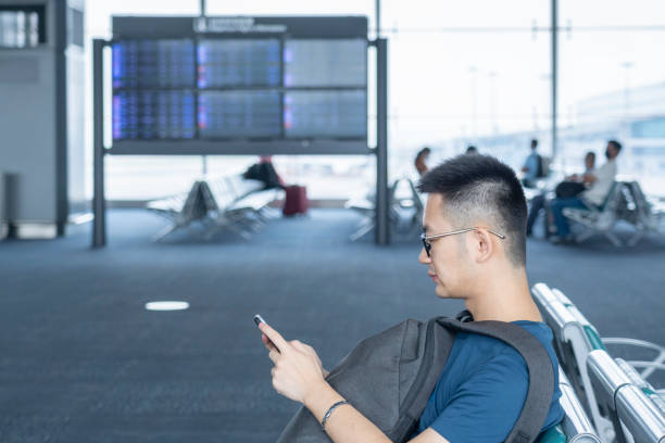 istock An Asian man with a backpack sitting and using his mobile phone in front of a Flight Information Screen in the airport 1280288887