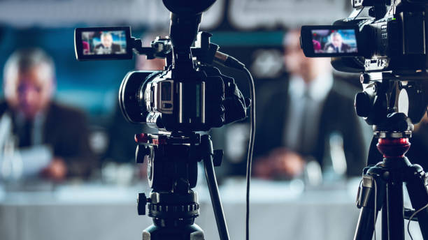 istock Two Cameras Recording Presentation At Press Conference, Blurred Speakers Wearing Suit Background 1280292060