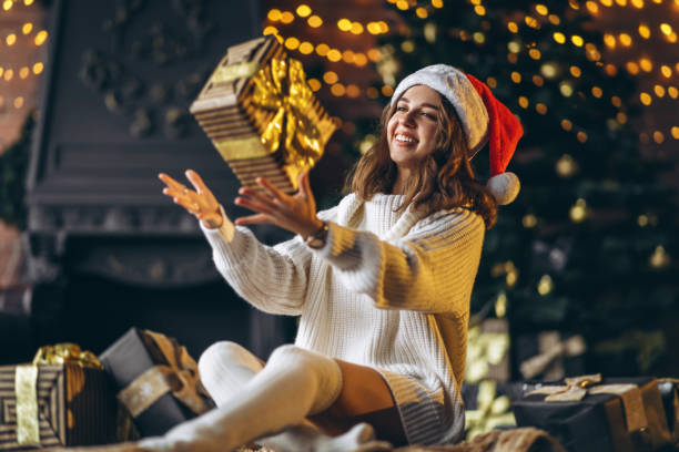 Pretty woman in warm sweater, socks and christmas hat, sitting on the floor at home with gift boxes stock photo