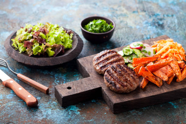 Grilled burger cutlets with baked sweet potato, vegetables and salad Grilled burger cutlets with baked sweet potato, vegetables and salad served on wood chopping board, selective focus paleo diet photos stock pictures, royalty-free photos & images