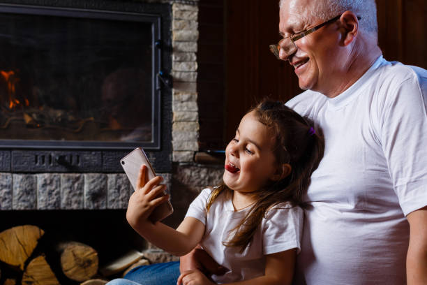 grand-père aîné et petite-fille mettant en vedette aux smartphones à l’intérieur - staring photos et images de collection