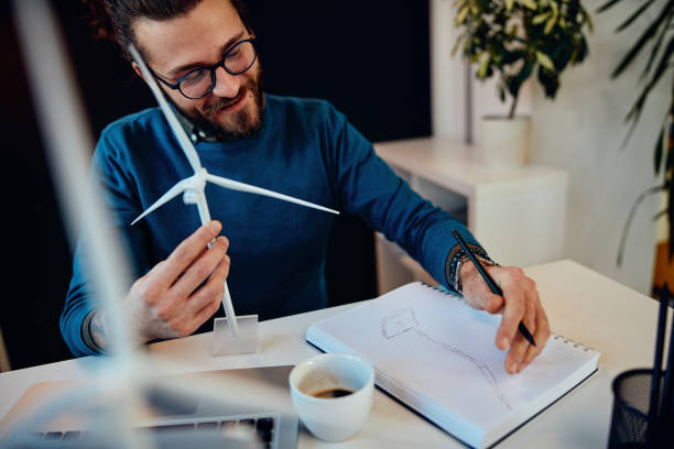 istock Young attractive bearded innovative ecology engineer holding windmill model and drawing. Sustainable development concept. 1280307437