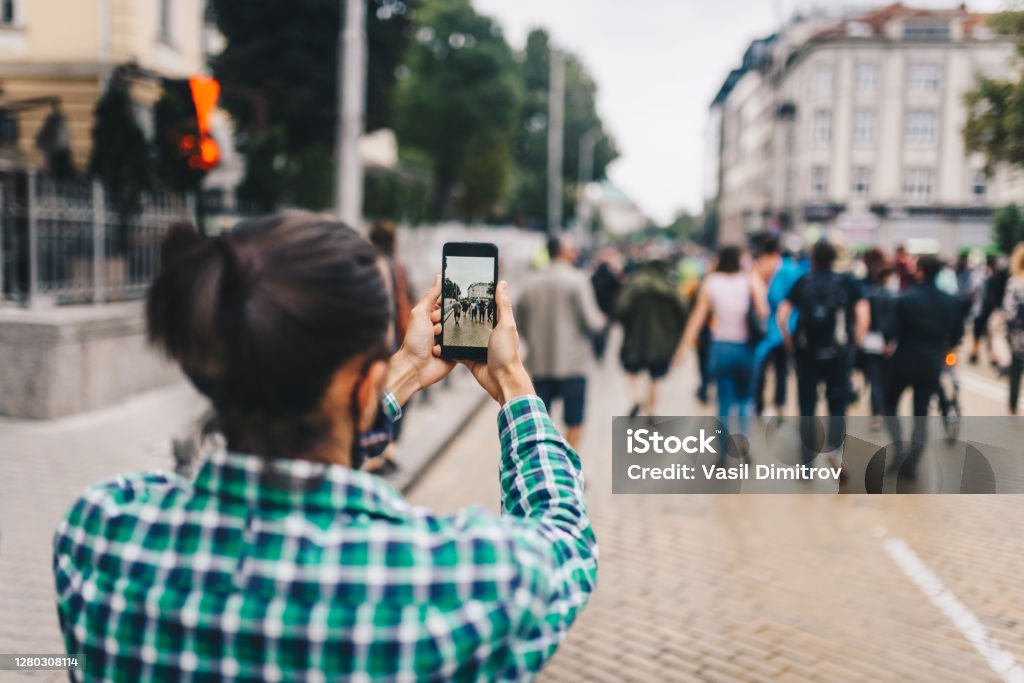 Young man recording a video / taking a photo of a crowd of people. 
Protest / procession in the city. Mobile journalism concept. Journalist Stock Photo