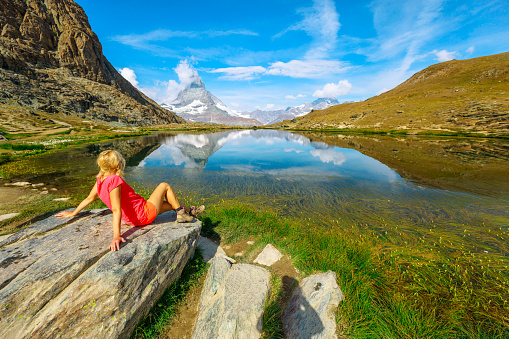 Mount Matterhorn reflected on Riffelsee Lake. Tourist woman relaxing after trekking from Rotenboden station on Gornergrat Bahn cog railway. Tourism in Zermatt, Canton of Valais, Switzerland.