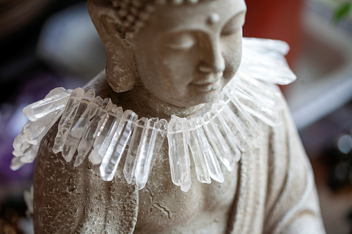 Close up detail still life of Buddha statue with crystal quartz necklace