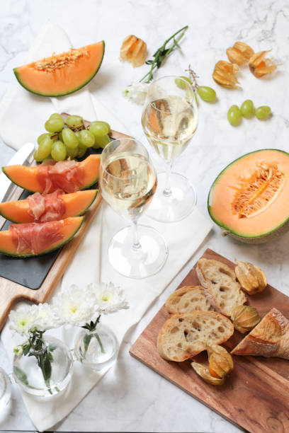 Food Flatlay with melon and prosciutto ham appetizer with wine Flatlay Melon and prosciutto ham appetizer with white wine and grapes vibrant color lifestyles vertical close up stock pictures, royalty-free photos & images