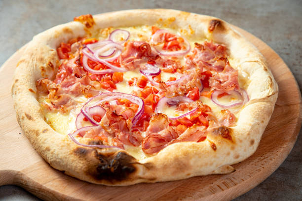 istock Pizza with mozzarella cheese base, ham, chopped cherry tomato and onion rings on peel 1280309561