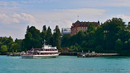 Mainau Island, Baden-Wuerttemberg, Germany - 07/14/2018: Passenger ferry ship arriving at landing stage of flower island Mainau, Lake Constance with castle in background.