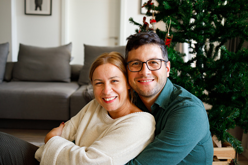 Couple in the living room hugging and posing in front of the Christmas tree.