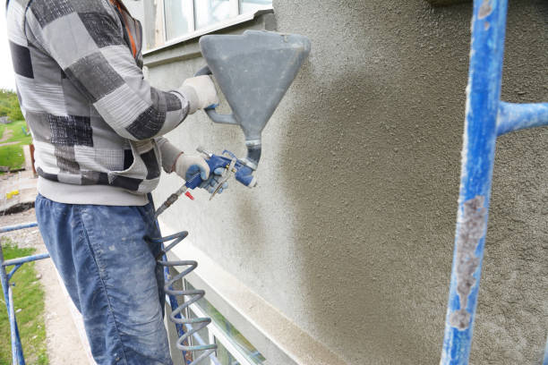 un imprenditore edile sta rendendo, intonacato, rivestimento la parete esterna di un edificio utilizzando una macchina spruzzatrice in gesso, pistola spruzzatrice in calcestruzzo stucco. - stucco building foto e immagini stock