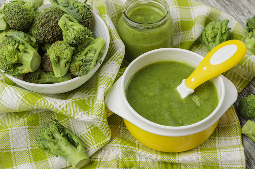 Fresh broccoli in the bowl, and portion of puree made from crushed, boiled broccoli, blurred background