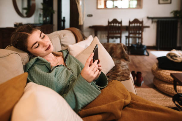 istock Young woman sitting on sofa and using phone 1280325556