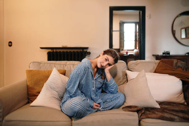istock Young woman wearing pajamas sitting on sofa 1280325676