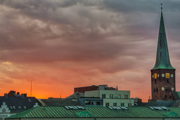 City skyline at sunset captured from the popular Dokk1 plaza with the Domkirke (Cathedral) bell tower standing out from the houses ' roofs featuring a medieval architectural style - Aarhus, Denmark