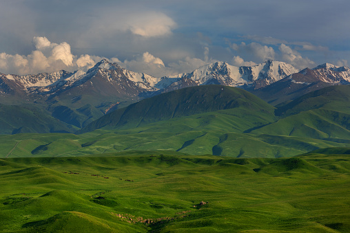 Picturesque hilly landscape on a plateau against the backdrop of a mountain range and cloudy sky in the northern Tien Shan