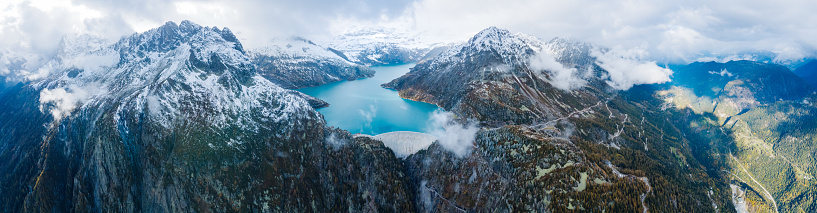 Panorama of arch dam and reservoir lake in snow covered Swiss Alps mountains to produce renewable energy from hydropower, sustainable hydroelectricity, aerial drone view, cold autumn weather