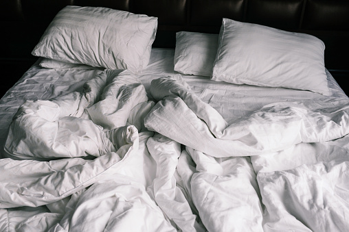 Unmade empty bed with white linens. Sheets and pillows in the apartment or hotel after a night's sleep. Dirty and crumpled blanket in the hotel.
