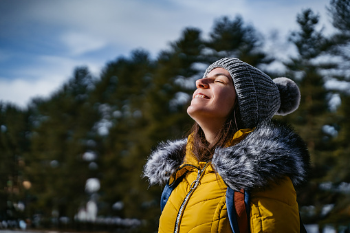 Beautiful young woman with closed eyes enjoying sunlight on snowy mountain.