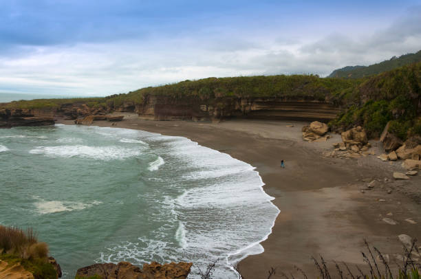 Volcanic beach with dark sand on low tide with waves crashing the shore on gloomy day with dramatic sky Scenic seascape of beautiful nature of New Zealand on Truman Track near Punakaiki punakaiki stock pictures, royalty-free photos & images