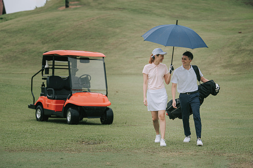Asia Chinese young couple golfer using umbrella on the golf course in rainy day