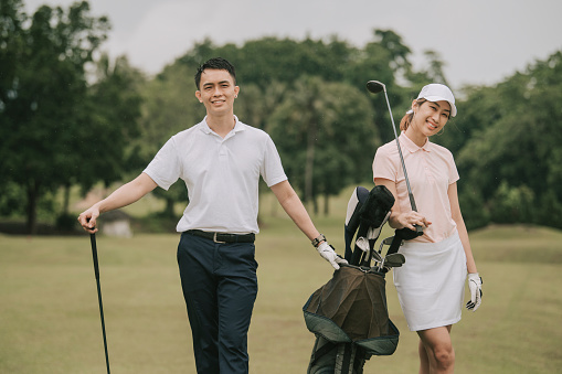 asian chinese young couple golfer posing in front of camera looking and smiling at camera in melaka golf course