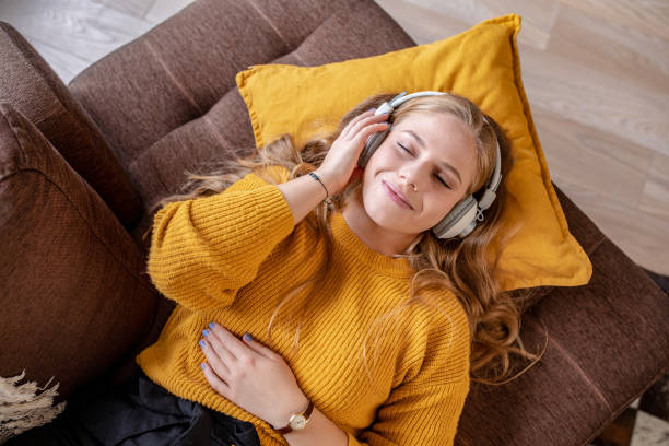 Young woman relaxing at home and listening music Photo of young woman with headphones laying on the couch and smiling headphones stock pictures, royalty-free photos & images