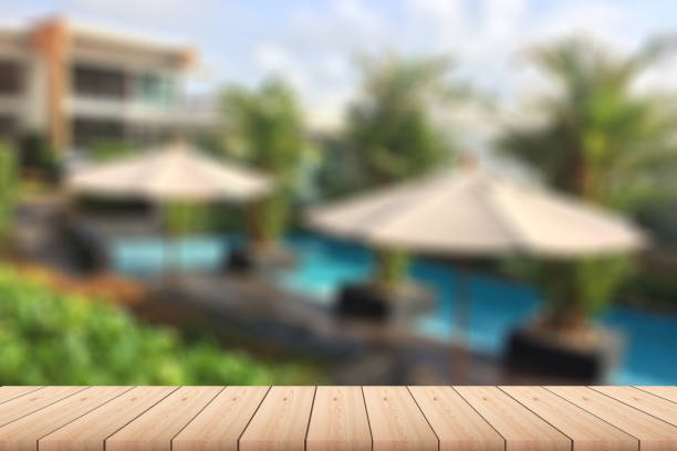 istock Empty wood plank table top with outdoor pool, trees, umbrellas and building with blur background - For product display. 1280341288