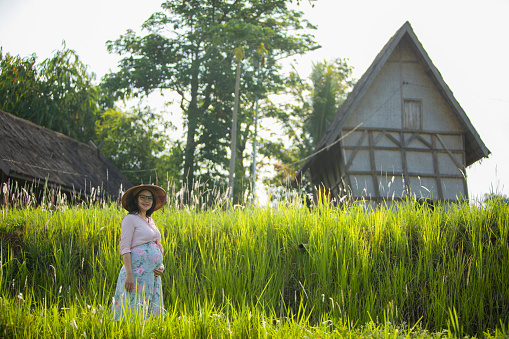 asian pregnant woman at  paddy field and her traditional house in cianjur district, West Java