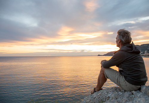 Man looks out to sea from coastal area at sunrise