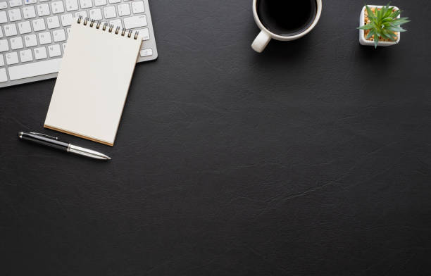 istock Black leather office desk table with keyboard, notebook and coffee cup with equipment other office supplies. Business and finance concept. Workplace, Flat lay with blank copy space. Top view 1280347443