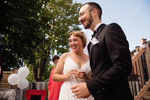 Millennial newlywed couple at wedding cocktail party in backyard. This is part of a series of a real wedding during Covid-19. Horizontal outdoors waist up shot with copy space.