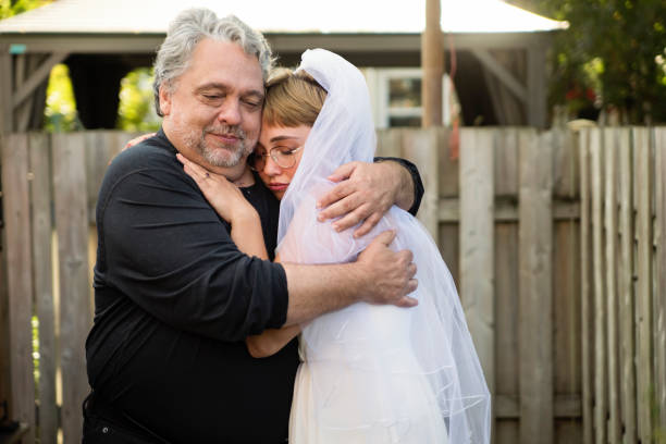 Millennial bride posing with father at wedding cocktail in backyard. Millennial bride posing with father in backyard during wedding cocktail party. This is part of a series of a real wedding during Covid-19. Horizontal outdoors waist up shot with copy space. bride hugging father on wedding day stock pictures, royalty-free photos & images
