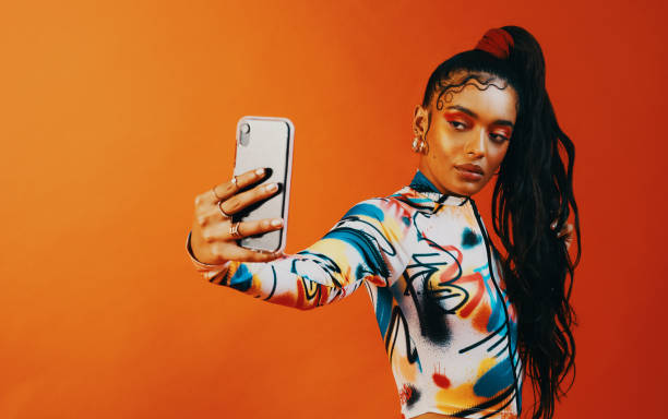 Let's start a baby hair challenge! Studio shot of a fashionable woman taking a selfie against a orange background fashion style stock pictures, royalty-free photos & images