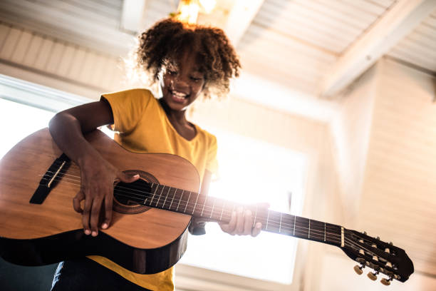 Child learning guitar playing skills while teacher guides hand placement, concentrating on technique and form in an indoor setting without natural light