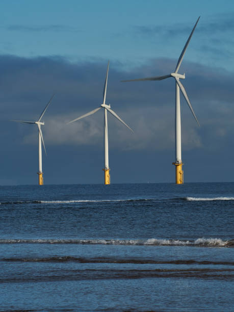Redcar 6 Image of a trio of near-shore wind turbines, lit by sharp winter sun, with a background of looming, threatening clouds and a foreground of sea and breaking waves. teesside northeast england stock pictures, royalty-free photos & images