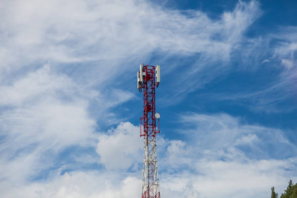 une tour cellulaire faite de métal rouge et blanc contre un ciel bleu avec des nuages blancs dans les montagnes de l’altaï sur un fond de cimes d’arbres verts pour la diffusion d’un signal sur les ondes radio pour les téléphones. - sky tree audio photos et images de collection