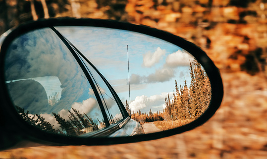 Looking  through the side view mirror of the car while traveling through The Yukon landscape in fall colors.