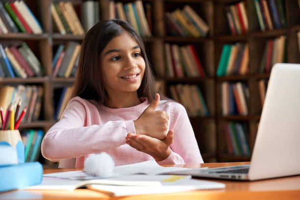 lächeln dinisch lateintauben behinderte kind schule mädchen lernen online-klasse auf laptop kommunikation mit lehrer per video-konferenz-anruf mit gebärdensprache zeigt handgeste während des virtuellen unterrichts. - deaf stock-fotos und bilder