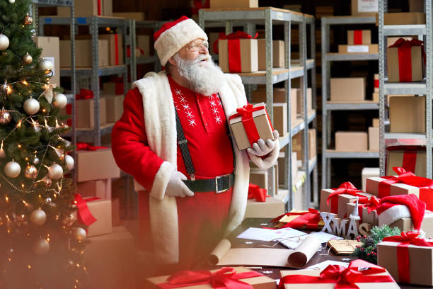 Happy old bearded Santa Claus wearing costume holding present gift box preparing for Merry Christmas standing in workshop looking through window waiting for New Year dreaming of xmas eve holiday time. feliz viejo y barbudo santa claus con traje sosteniendo la caja de regalo actual preparándose para feliz navidad de pie en el taller mirando a través de la ventana esperando año nuevo soñando con el tiempo de vacaciones de la víspera de navidad.