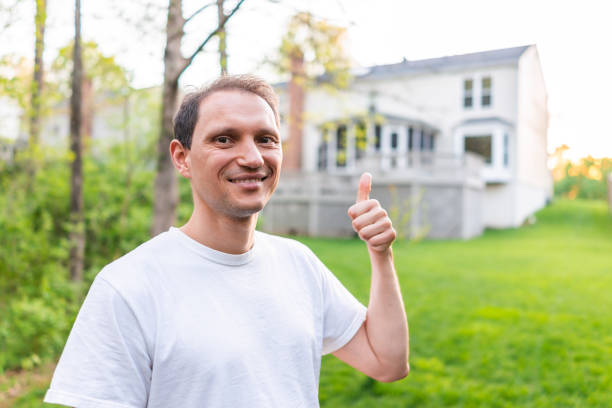 Young man happy homeowner in Herndon, Northern Virginia, Fairfax county residential neighborhood in spring or summer house backyard pointing with thumb Young man happy homeowner in Herndon, Northern Virginia, Fairfax county residential neighborhood in spring or summer house backyard pointing with thumb herndon virginia stock pictures, royalty-free photos & images