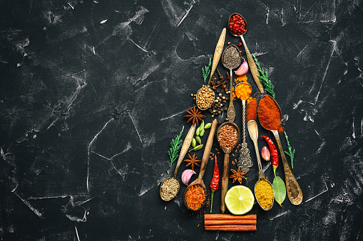 Abstract Christmas tree made from spices in spoons on a black stone background. Top view, flat lay, copy space