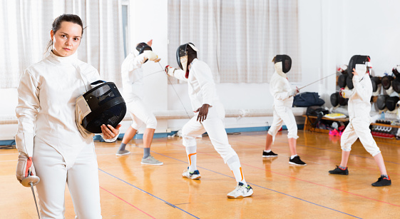 Portrait of smiling sporty young cheerful positive glad woman with foil at fencing workout