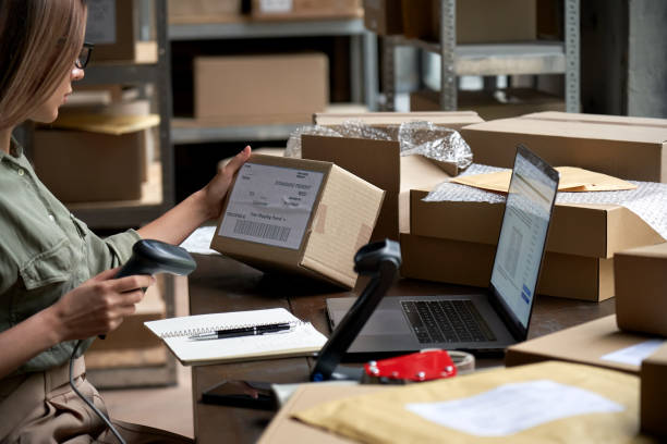 istock Female seller worker online store holding scanner scanning parcel barcode tag packing ecommerce post shipping box checking online retail store orders in dropshipping delivery service warehouse. 1280366033
