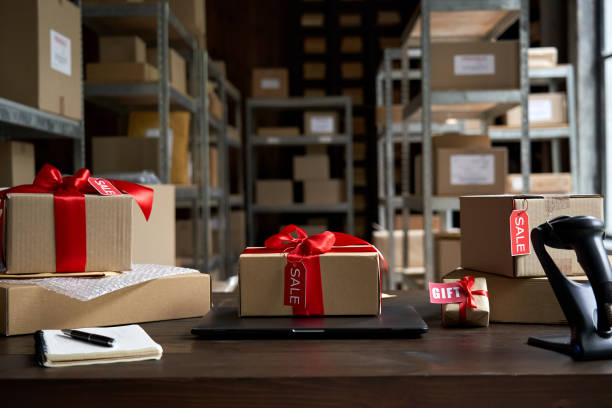 Table with laptop and gift boxes with sale tags on table in warehouse. Online ecommerce retail business black friday discounts deals, free shipping. Best buy holiday offers concept storage background. mesa con portátil y cajas de regalo con etiquetas de venta sobre mesa en almacén. negocios de comercio electrónico en línea de negocios negros viernes descuentos ofertas, envío gratuito. las mejores vacaciones de compra ofrecen un fondo de almacenamie