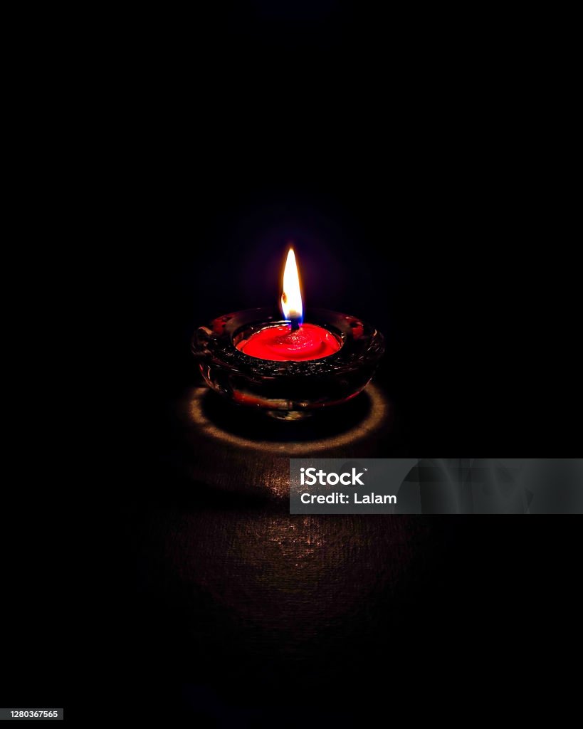 Isolated,close up image of small red colored wax lamp(Diya) burning in dark night with steady yellow,blue flame. Black Color Stock Photo