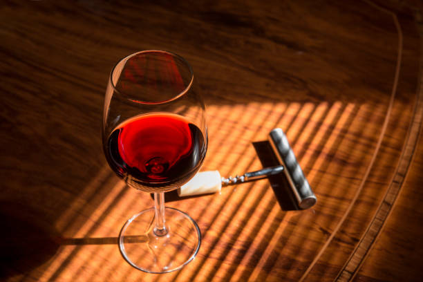 glass of red wine with metal corkscrew on wooden table and natural light close-up of red wine glass on table with corkscrew with shades of a blind rioja photos stock pictures, royalty-free photos & images
