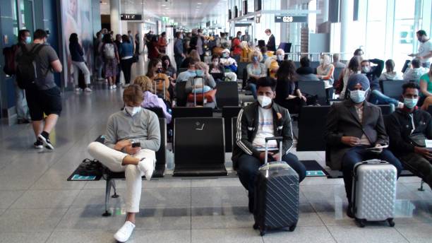 People Wearing Face Mask Due To COVID-19 Pandemic, Waiting For Airplane Boarding At Munich Airport In Bavaria Germany. Europe Scene Of People Sitting Down, Standing, Looking Around, Talking To One Another, Wearing Face Mask Due To Coronavirus Pandemic, Getting Ready To Board Passengers Airplane At Munich International Airport In Bavaria Germany Europe munich airport stock pictures, royalty-free photos & images