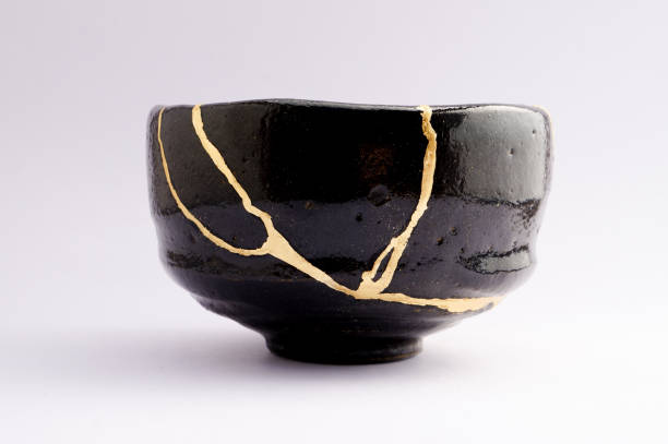 Antique broken Japanese raku black bowl repaired with gold kintsugi technique Kintsugi black raku bowl. Gold cracks restoration on old Japanese pottery restored with the antique Kintsugi restoration technique. The beauty of imperfections. japanese pottery repair gold. japanese art of repairing cracks with gold. japanese art of fixing broken pottery imperfection stock pictures, royalty-free photos & images