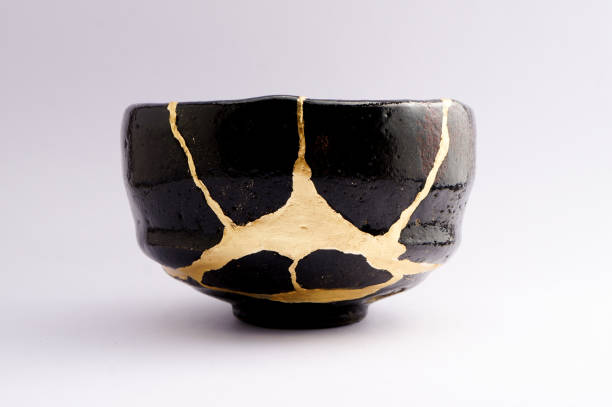 Antique broken Japanese raku black bowl repaired with gold kintsugi technique stock photo